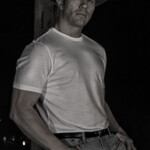 Man wearing cowboy hat leaning against wooden post