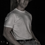 Man wearing cowboy hat leaning against wooden post