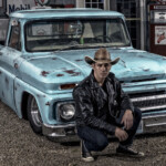 Man in cowboy hat by vintage blue pickup