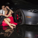 Couple embracing beside luxury car in red dress