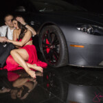 Couple embracing beside luxury car in red dress