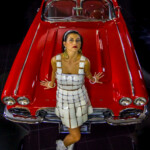 Model leaning against shiny red classic car