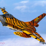 Tiger-striped fighter jet flying over clouds