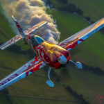 Red aerobatic plane trailing smoke over fields