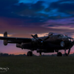 WWII bomber silhouetted against dramatic sunset sky