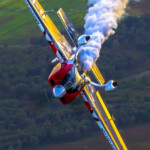 Red aerobatic plane trailing smoke over countryside