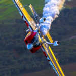 Red aerobatic plane trailing smoke over countryside