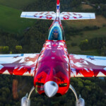 Red aerobatic airplane with pilot over fields