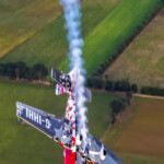 Aerobatic airplane trailing smoke over farmland