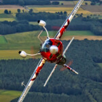 Red aerobatic plane banking over rural landscape
