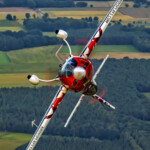 Red aerobatic plane banking over rural landscape